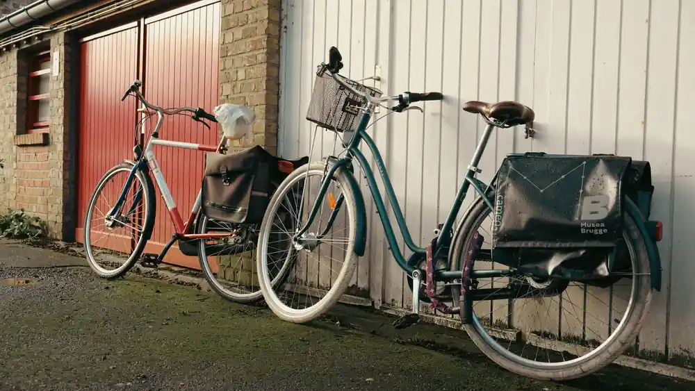 Two bicycles with panniers leaning against a wall on a wet day