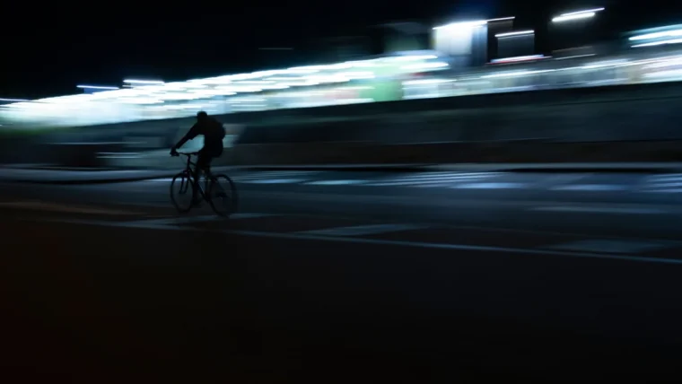 Cyclist commuting at night on a lit urban road with front and rear bike lights visible