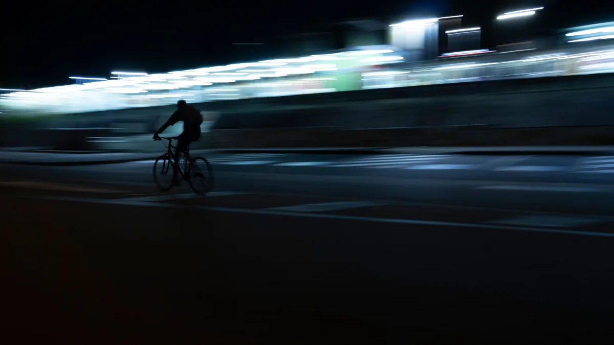 Cyclist commuting at night on a lit urban road with front and rear bike lights visible