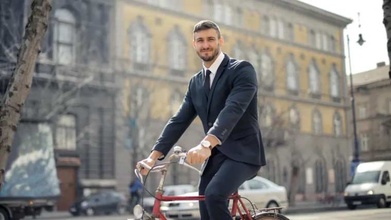 A man in a dark suit riding a red bicycle