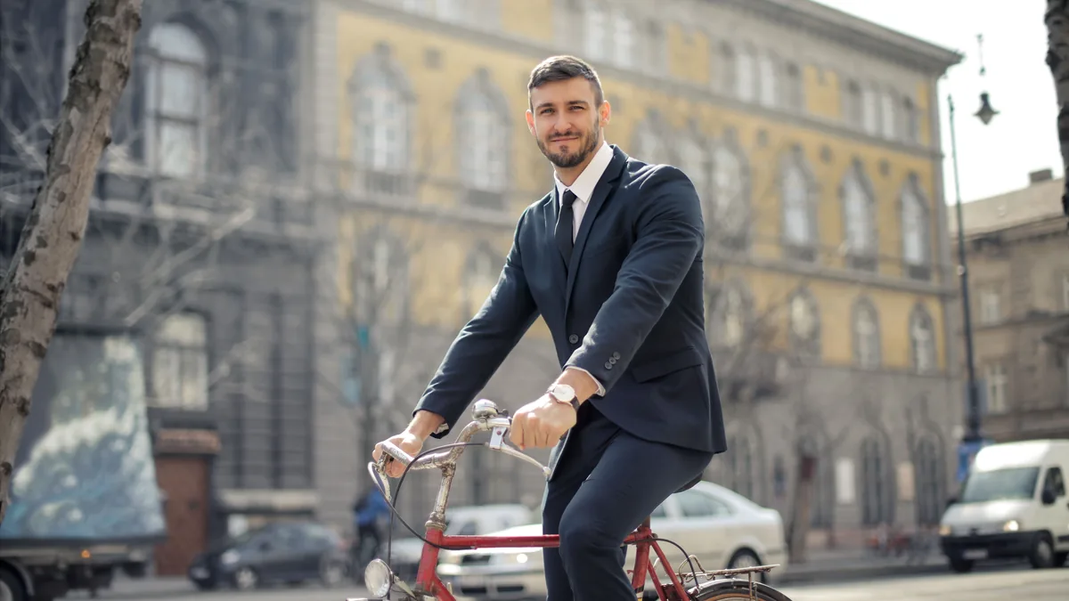 A man in a dark suit riding a red bicycle