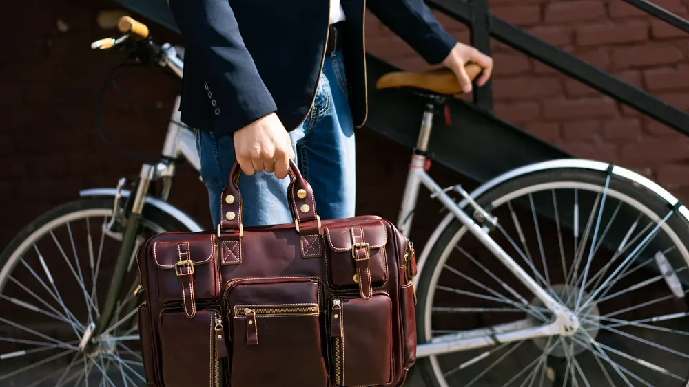 A person in a suit jacket holding a leather briefcase beside a bicycle