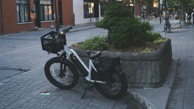 A white e-bike with a front basket and rear pannier parked on a paved city street