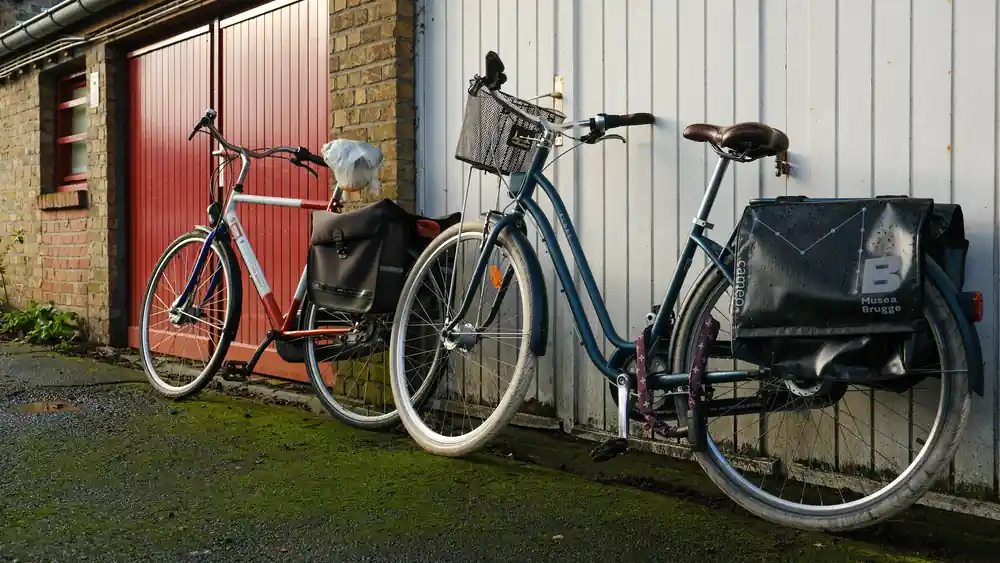 Two town bikes with pannier bags, a front basket and a lock, parked against garage doors