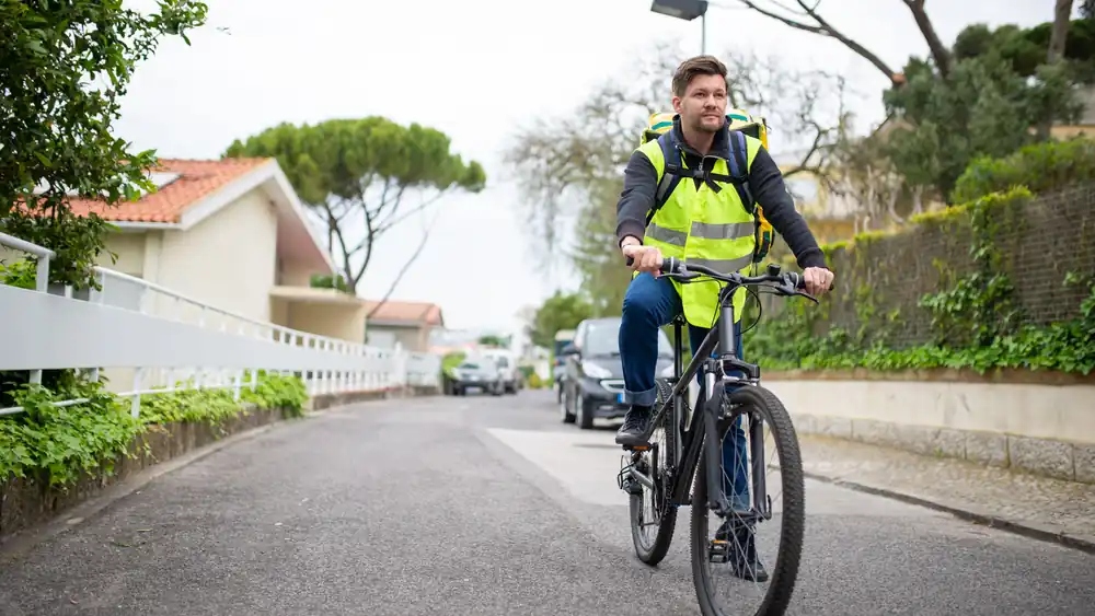 A cyclist in a high-visibility vest riding along a quiet residential street