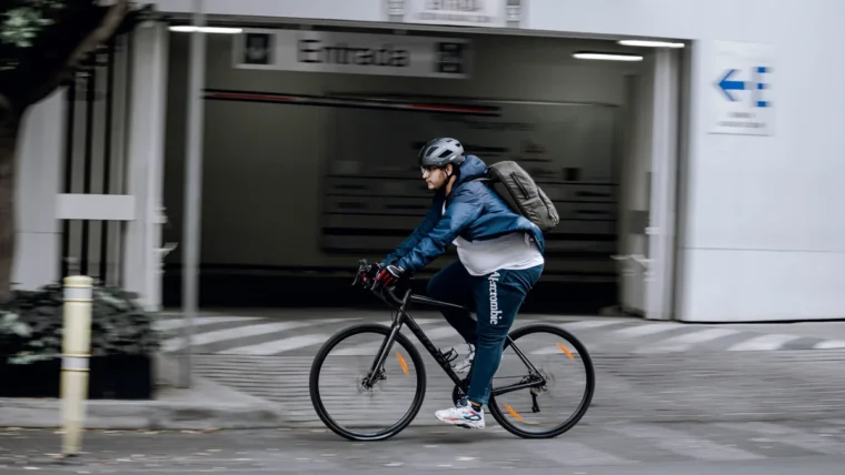 A commuter in a helmet and rucksack riding a black hybrid bike along a city street