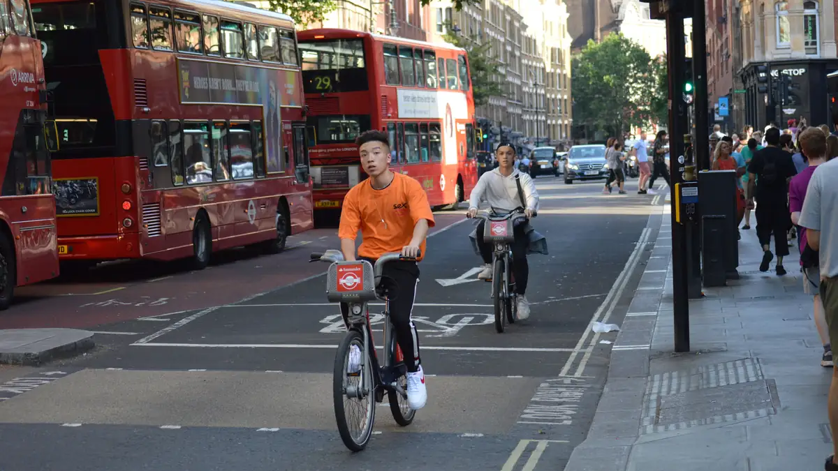 Two cyclists riding past red double-decker buses on a London street