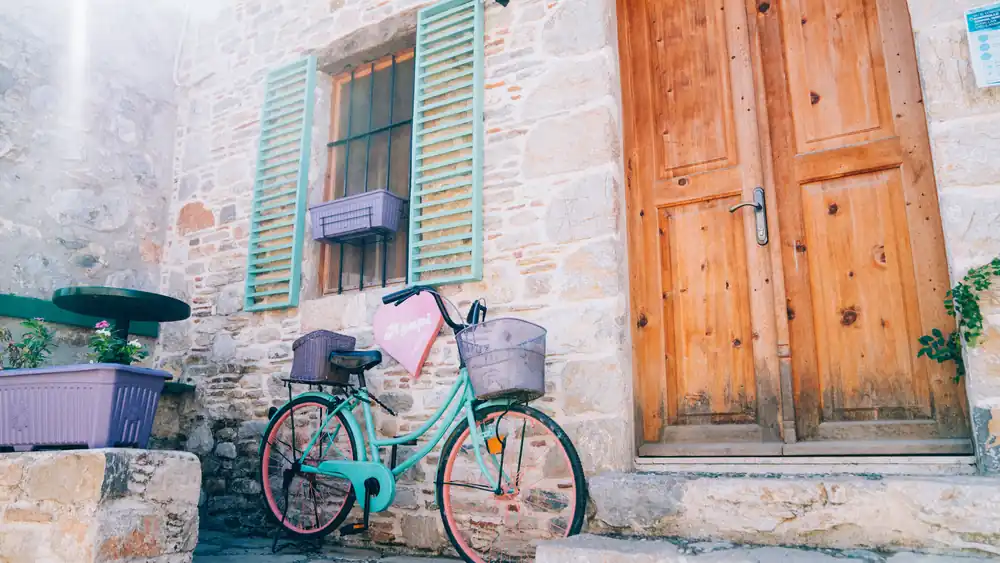 A bicycle with front and rear baskets parked outside the door of a stone house